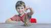 Chłopiec układa wieżę z zaoszczędzonych monet. Ilustracja artykułu dla rodziców o kieszonkowym.